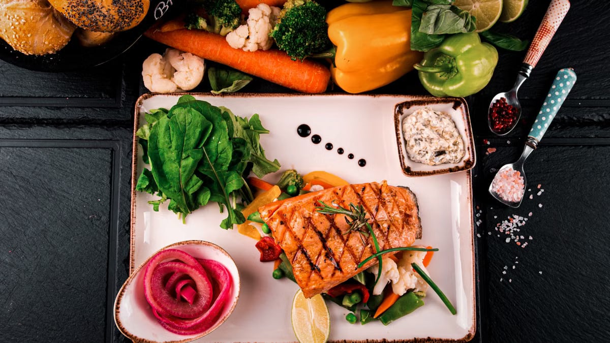 Top view of grilled salmon served with vegetables, herbs, and fresh bread. Perfect for a healthy meal.
